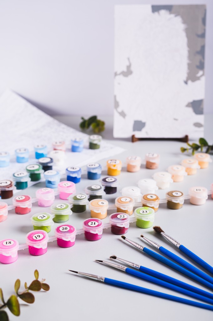 Paint by number kit with numbered paint pots, brushes, and canvas on an easel